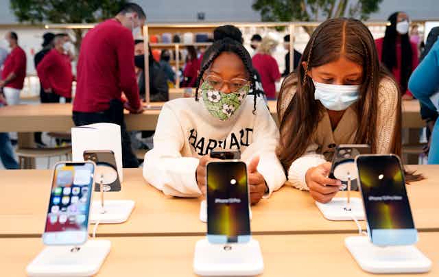 Two girls wearing masks hold and look at iPhones at an apple store