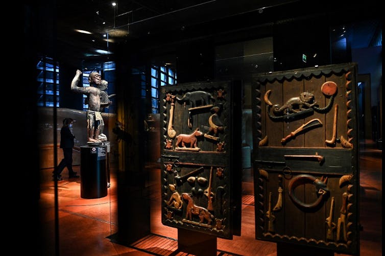 Portes de palais décorées et statue issues du trésor d'Abomey exposé dans des vitrines de musée.