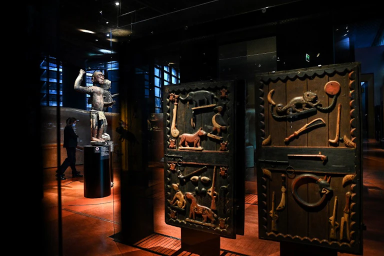 Portes de palais décorées et statue issues du trésor d'Abomey exposé dans des vitrines de musée.