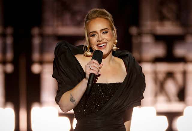 Adele smiles and holds a microphone