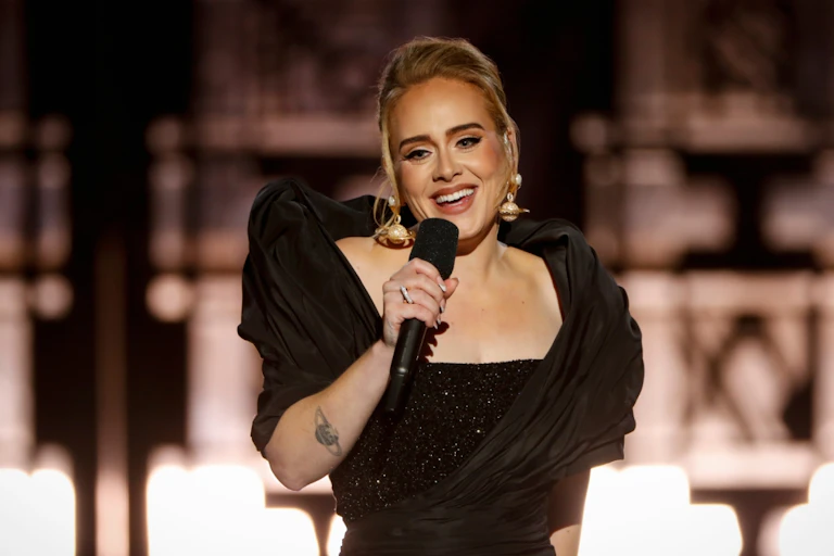 Adele smiles and holds a microphone