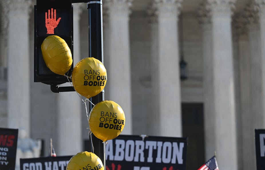 Balloons with "Bans off our bodies" float by a traffic signal outside the Supreme Court.