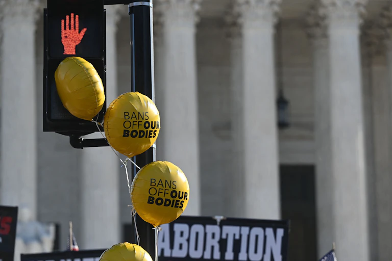Balloons with "Bans off our bodies" float by a traffic signal outside the Supreme Court.