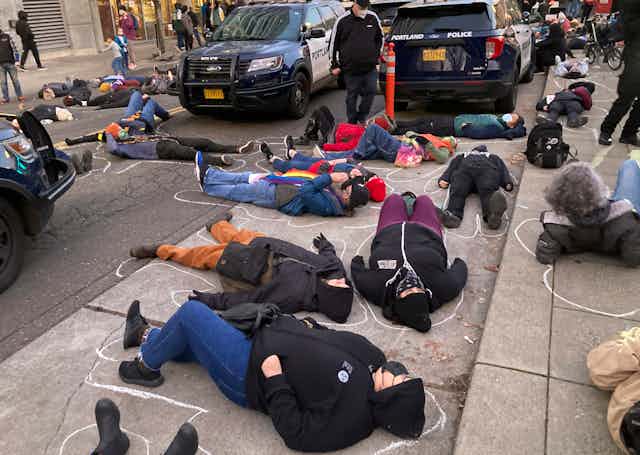 protestors lie in the street with chalk body outlines around them