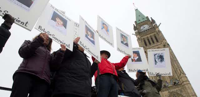 people hold signs remembering their lost loved ones with the peace tower behind them