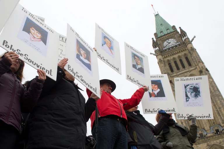 people hold signs remembering their lost loved ones with the peace tower behind them