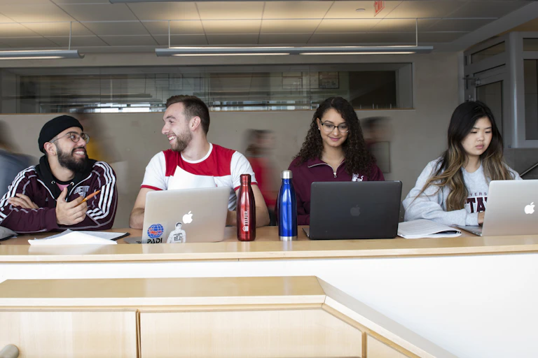 Students sittin at a long desk working on laptops