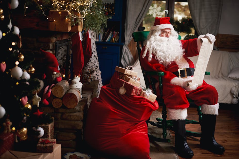 Portrait of Santa Claus, sitting in chair with sack full of presents, looking at a Christmas list.