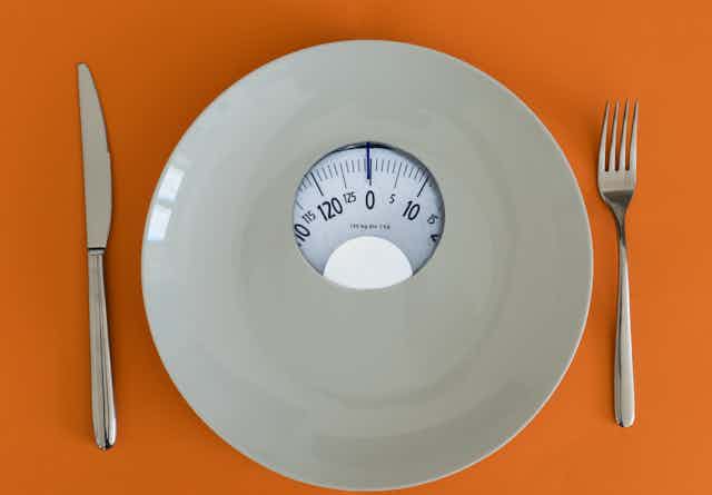 A plate with a weight scale in the middle, with a knife and fork on an orange background