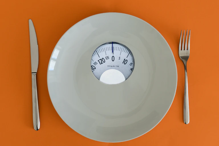 A plate with a weight scale in the middle, with a knife and fork on an orange background