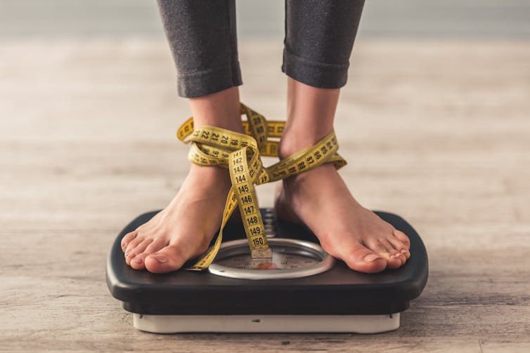 Feet on a scale, with a tape measure tangled around the ankles