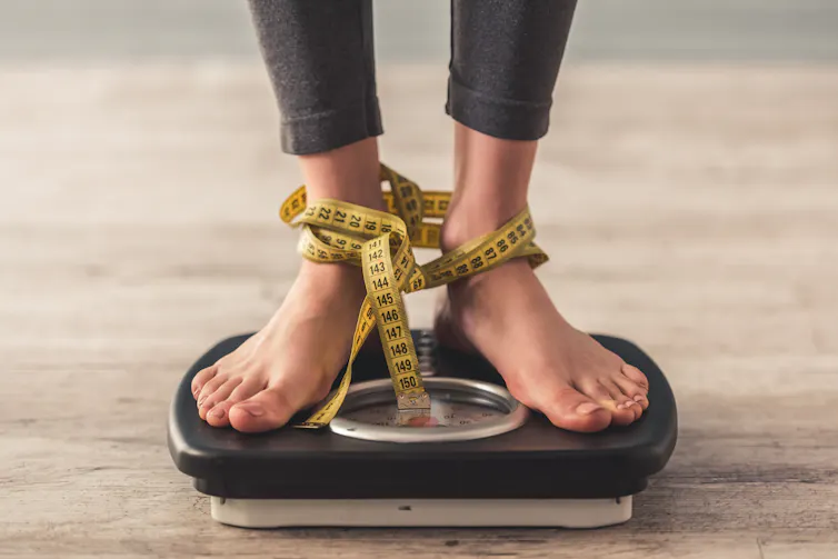 Feet on a scale, with a tape measure tangled around the ankles