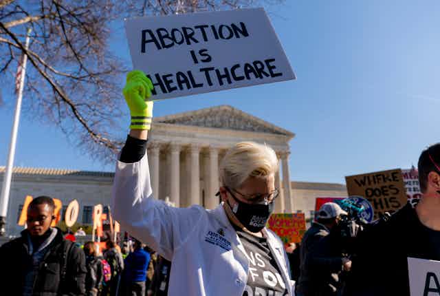 A woman holds up a sign saying abortion is healthcare during a protest in front of the Supreme Court, which is in the background