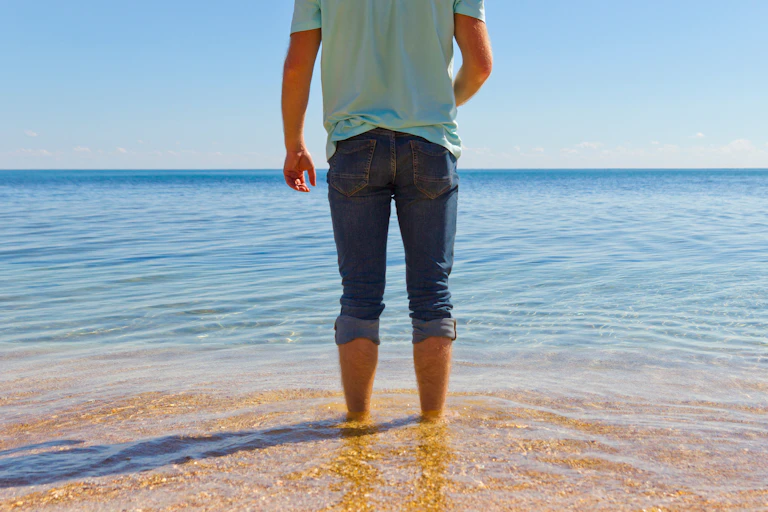 A man looks at the ocean but does not go in