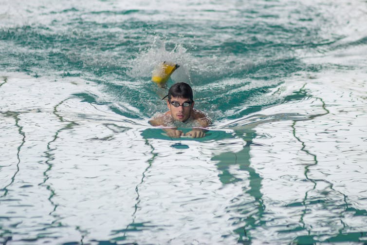 A man kicks in a pool with fins on.