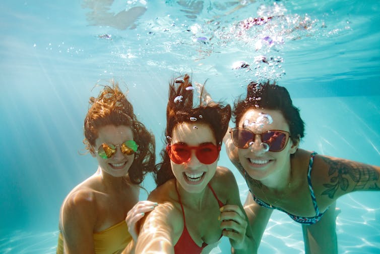 Three young women have fun underwater at the pool