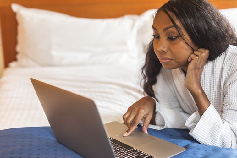 A person lies on their bed with a laptop.