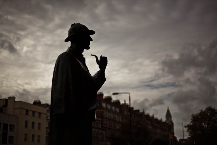 A photo of the Sherlock Holmes statue in London in silhouette against a grey sky and dark skyline