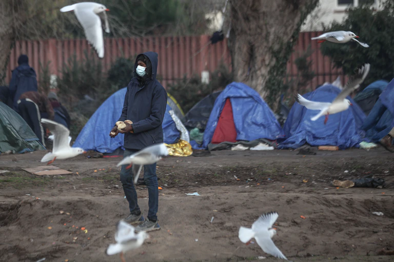 A young man holding bread at the centre of a flock of seagulls
