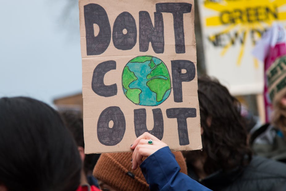 A protester holds a cardboard sign reading, 'don't cop out'.