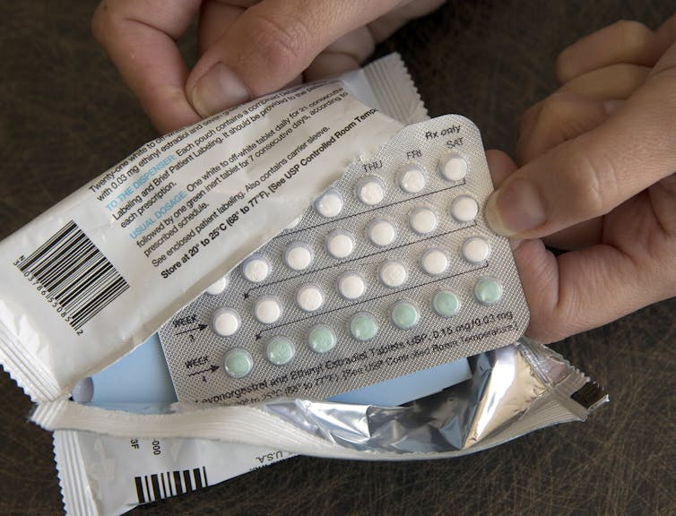 Two hands hold a package containing a one-month dosage of hormonal birth control pills