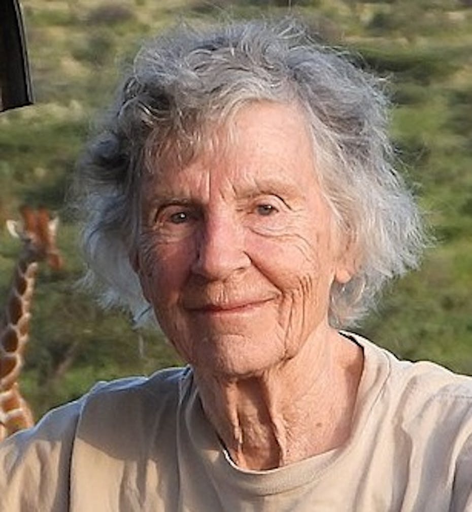 A woman is seen smiling with a giraffe behind her.
