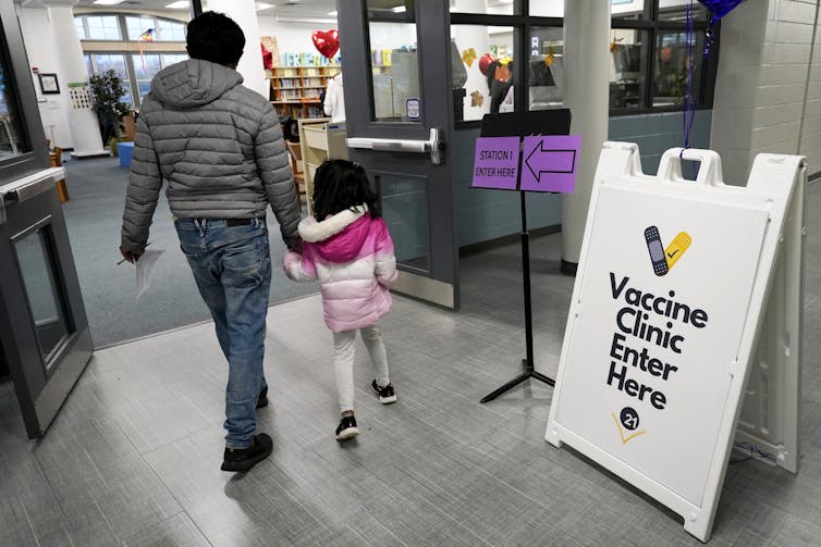 A man and a little girl in a pink jacket entering a vaccine clinic