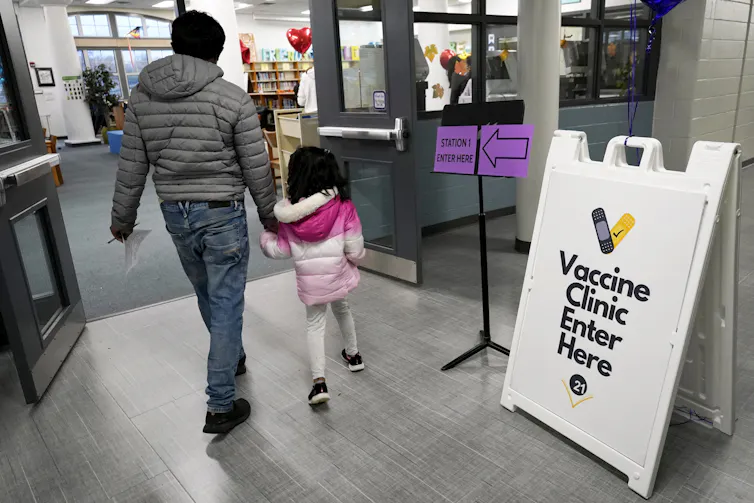A man and a little girl in a pink jacket entering a vaccine clinic