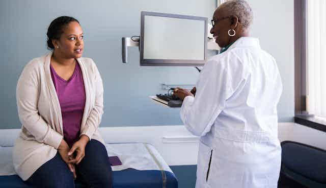 Smiling Black woman doctor talking with female Black patient in an exam room.