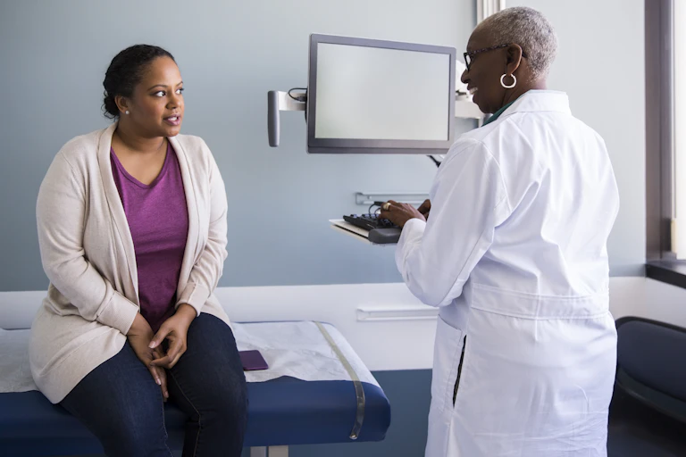 Smiling Black woman doctor talking with female Black patient in an exam room.