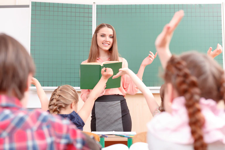Young teacher stands in front of class of children raising hands