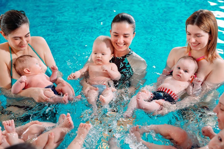 Babies and mothers play in a pool.