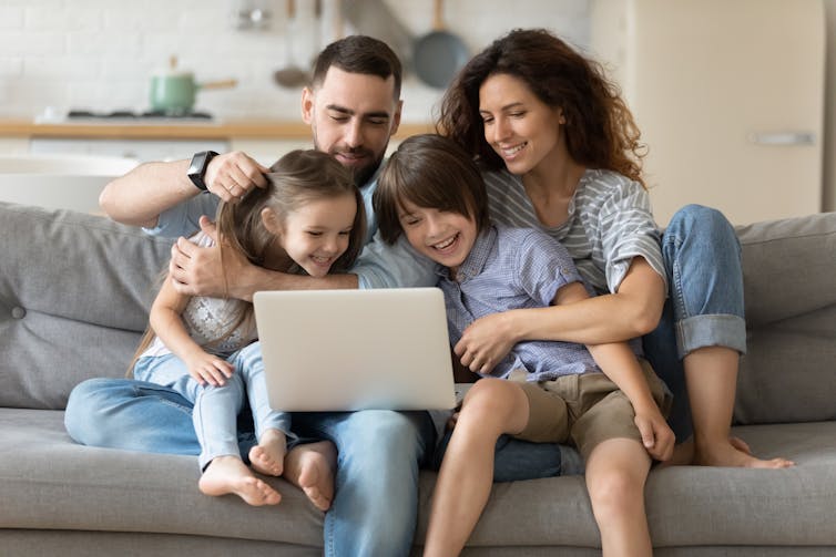 A family of four look at a laptop.