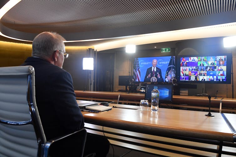 man sits at desk and looks at two TV monitors