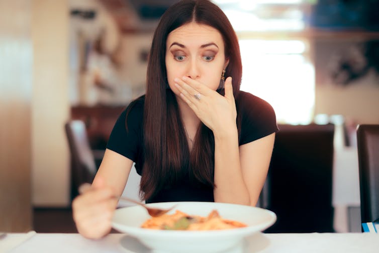 A woman covers her mouth while eating and looking full.