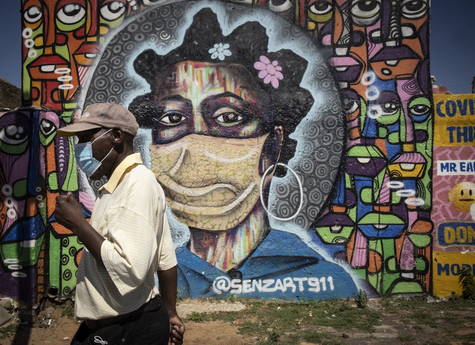 A man wearing a COVID-19 mask walks past graffiti showing a woman wearing a mask