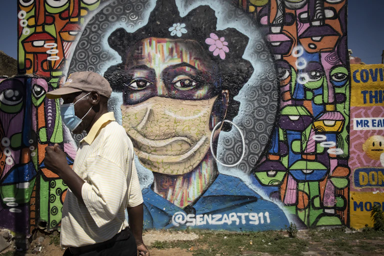 A man wearing a COVID-19 mask walks past graffiti showing a woman wearing a mask
