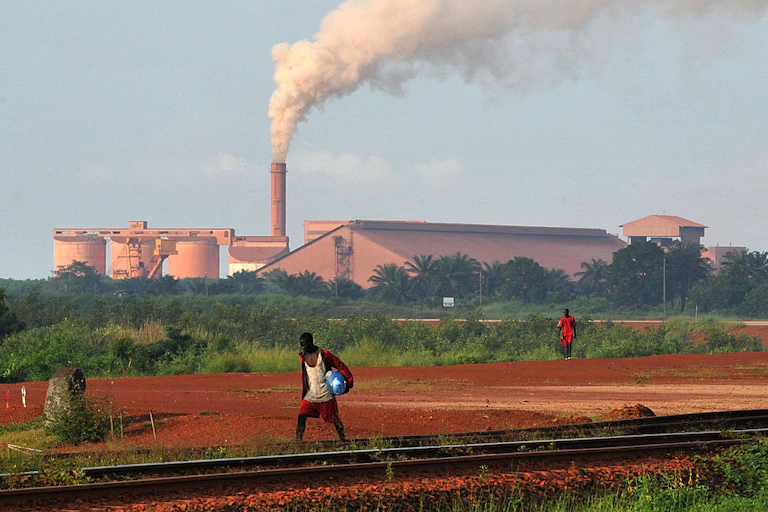 A man walks on rail track while smoke rises from a factory behind him.