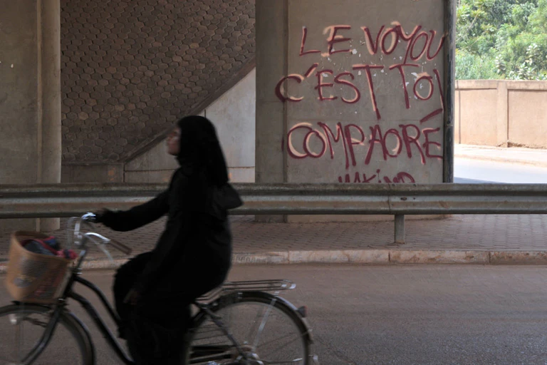 A woman rides a bicycle past graffiti on a wall