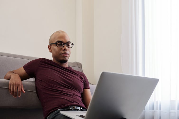 A man on his laptop, appears to be watching something.