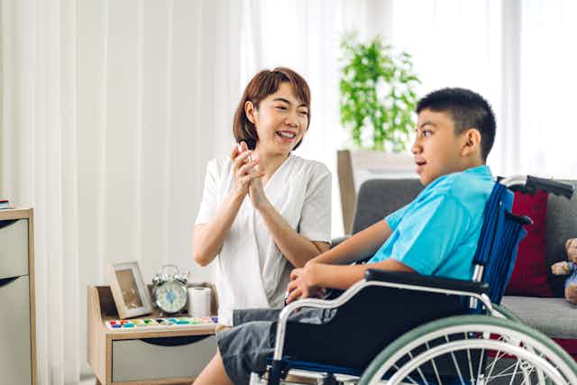 A carer sits with a young man in a wheelchair