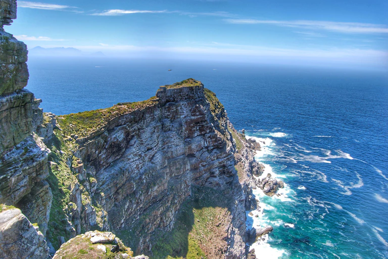 The edge of a mountain in the ocean with the blue sea meeting the sky in the background.