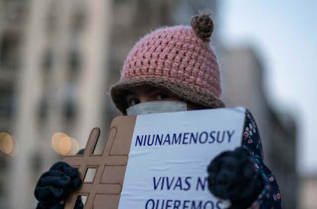 A girl wearing a face mask to prevent the spread of new coronavirus holds a sign that reads in Spanish "Not one less 