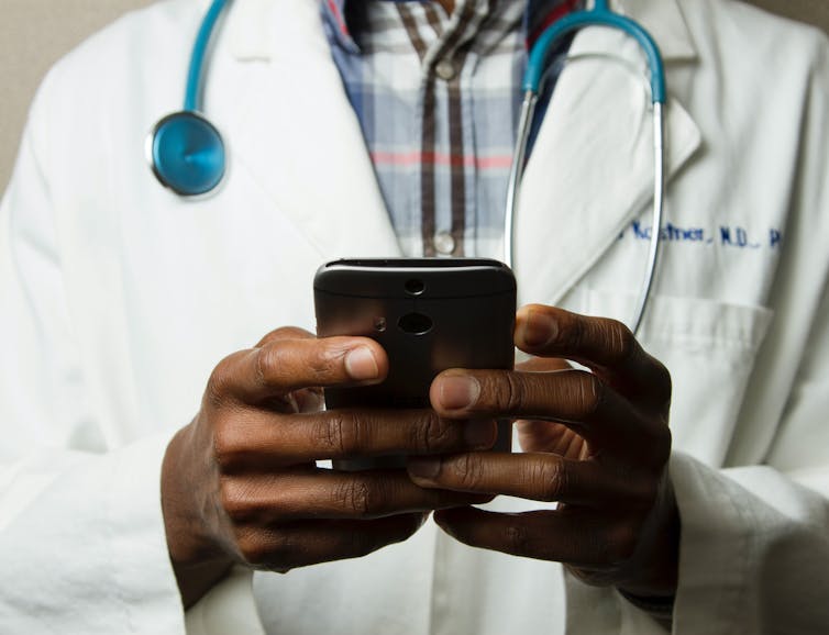 Cropped shot of man in white coat with stethoscope holding a smartphone in the foreground