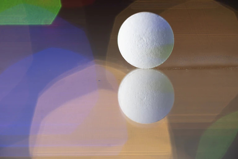 A white pill sits on a reflective surface.
