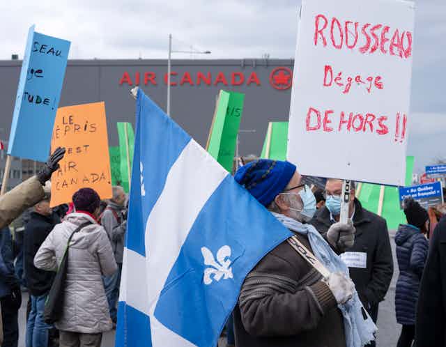 A man carries a fleur du lis and a sign condemning the CEO of Air Canada