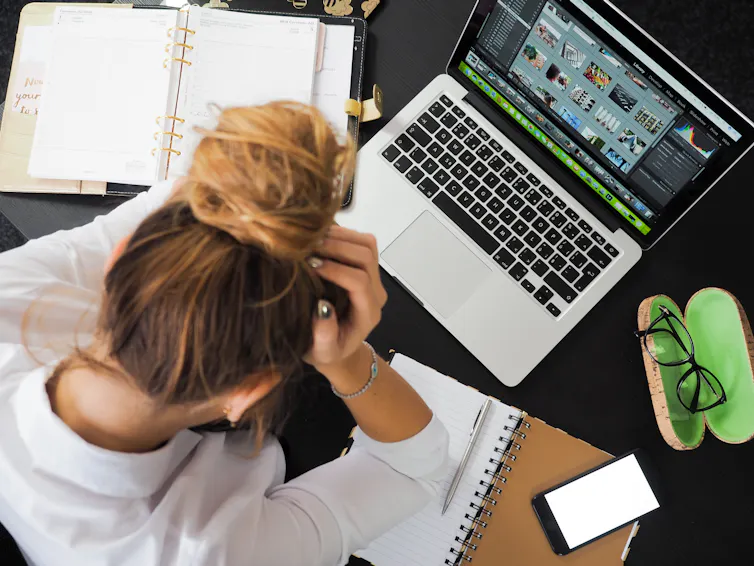 A woman sits at a laptop with her head in her hands.