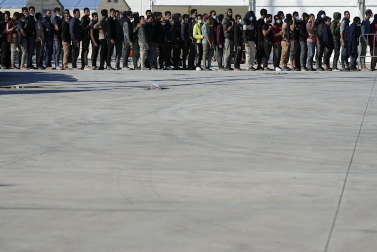 Hundreds of people stand in a long line.