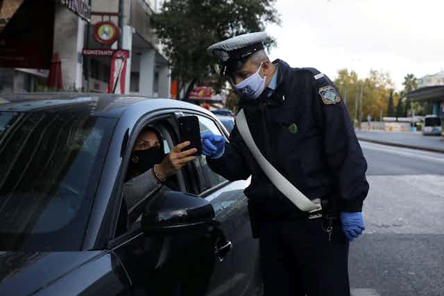 Greek policeman performs checks on a driver's documents verifying purpose of movement,