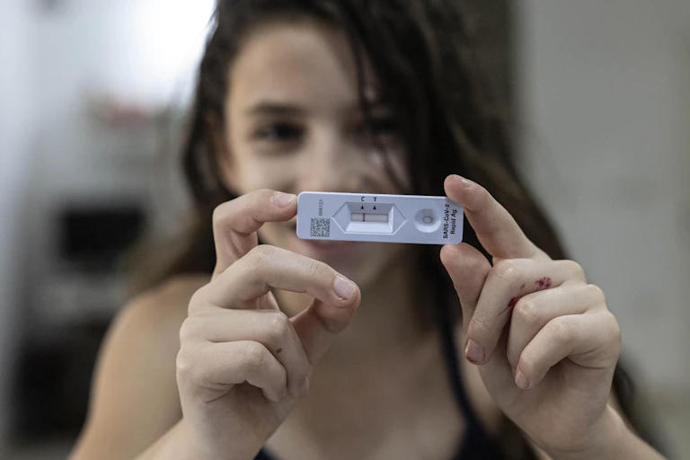 A girl out of focus in the background holding up a negative COVID-19 rapid antigen test in the foreground